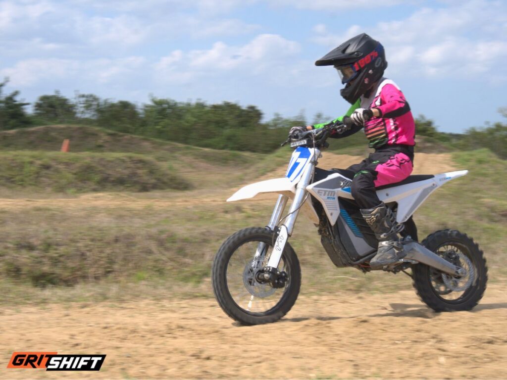A kid on an electric dirt bike wearing all the protective gear. 