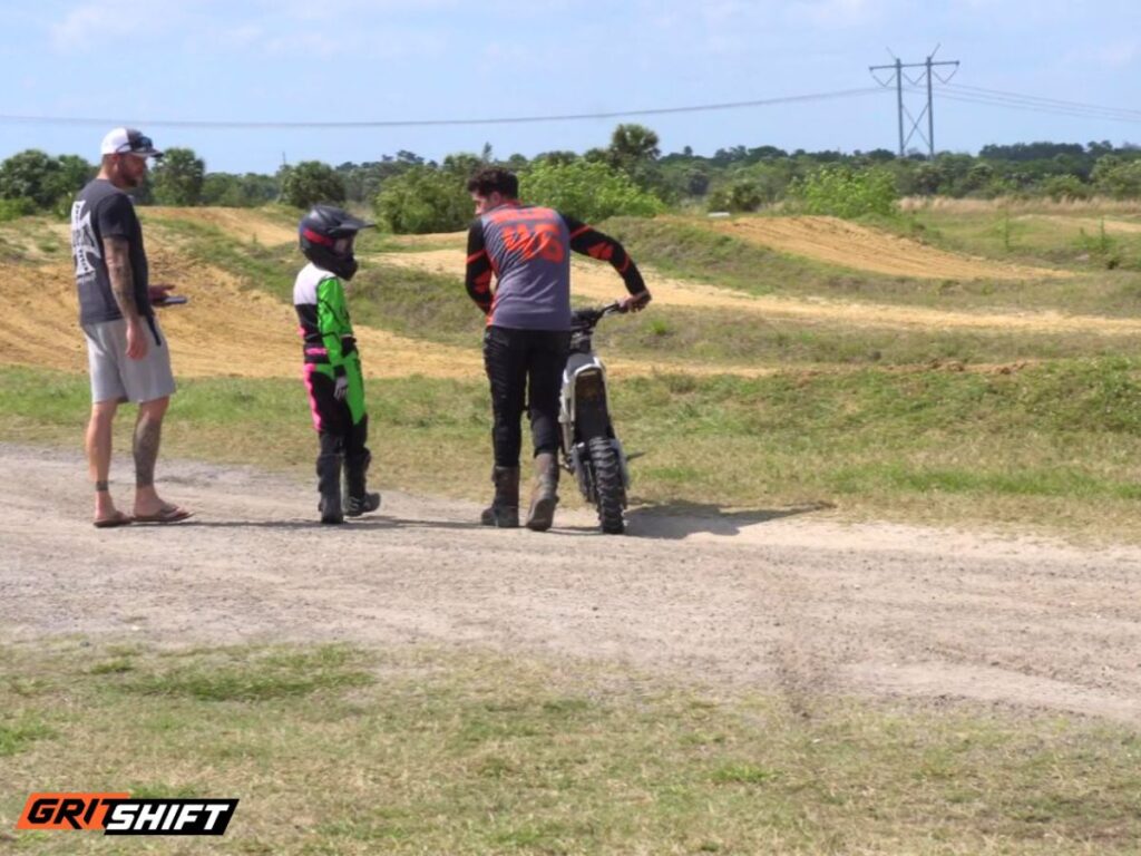 A child being mentored on how to start riding, standing next to the track.