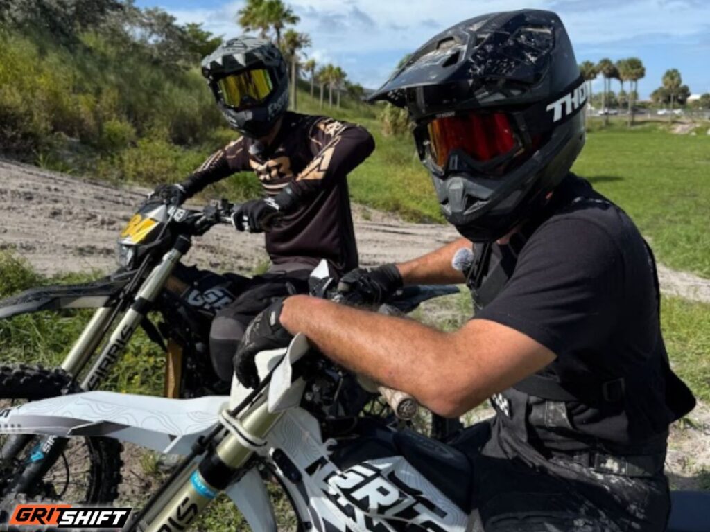 2 riders sitting on their emotos with a dirt track in the background